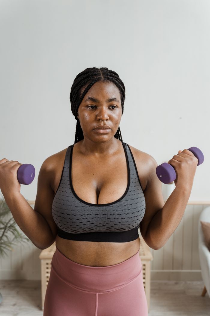 services-04 Confident woman in activewear lifting dumbbells indoors, focusing on fitness and strength training.